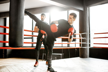 Athletic man kicking punching bag with leg, training kickboxing on the boxing ring at the gym