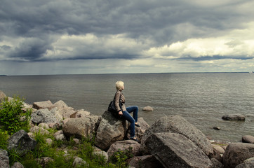 Fototapeta na wymiar Woman sitting on a rock and looking at the sea under the gloomy sky