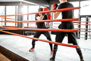 Two professional boxers in black sportswear during the fight on the boxing ring at the gym