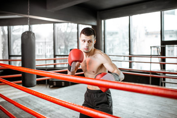 Young athletic man hard training to box, fighting on the boxing ring at the gym