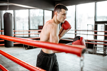 Young athletic man hard training to box, fighting on the boxing ring at the gym