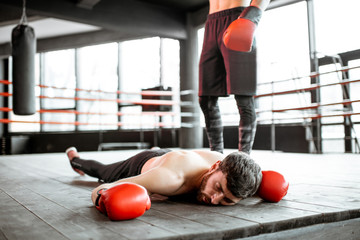 Beaten boxer lying on the floor during a boxing battle, having a knockdown on the boxing ring