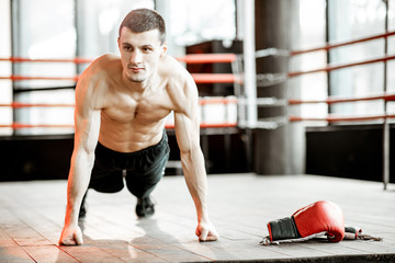 Portrait of a strong boxer showing muscles during the training on the boxing ring at the gym