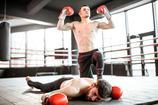Beaten boxer lying knocked out on the boxing ring with strong man winner above
