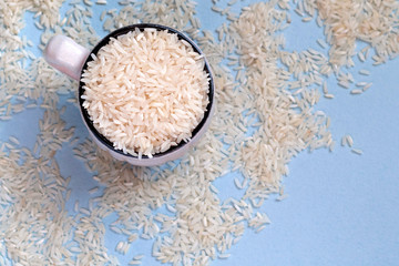 White uncooked rice in mug on blue background. Carbohydrates, healthy food. Place for text.