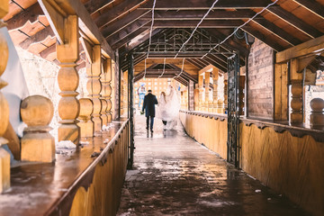 The bride and groom go into the distance along a wooden corridor. View from the back.