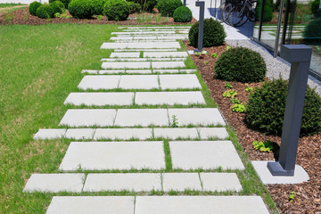 Moderner Gartenbau: Beleuchteter Gehweg umrahmt von Rasen, Ziersplitt und Buchsbäumen in mit Mulch...