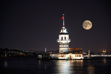 Fototapeta premium Kiz Kulesi or Maiden's Tower in Istanbul with beautiful city night and full moon. Old historical tower - in Turkey