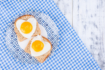 Romantic Breakfast of 2 fried eggs in the shape of a heart .. Valentine's Day concept. Wooden white background and napkin with a plate of food. Free space for text. Flat lay.
