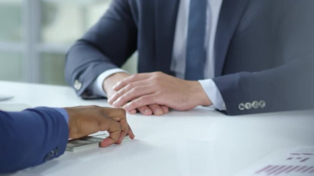 Close-up view of hands of businessman giving stack of money to African male coworker at office desk