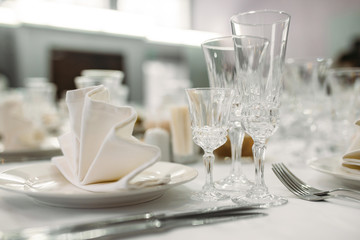 Luxury dinner set arranged on a table with vintage cream lace tablecloth and napkins, elegant porcelain dishes, silverware and crystal glassware