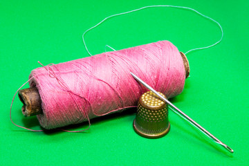 spool of thread, needle and thimble on a green background