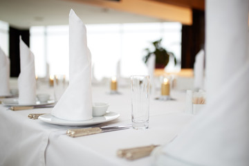 dinner set arranged on a table with vintage cream lace tablecloth and napkins, elegant porcelain dishes, silverware and crystal glassware