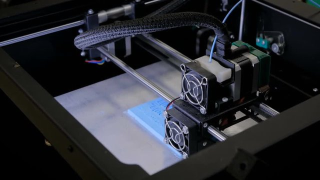 Print head of 3D printer machine printing flat plastic model at modern scifi technology exhibition. 3D printing, additive technologies, 4.0 industrial revolution and futuristic concept