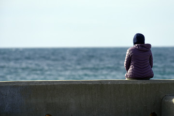 The girl sits on the pier and looks at the sea.