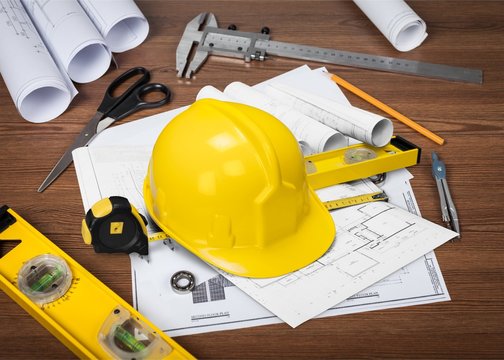Yellow hard hat and blueprints on wooden desk in a construction