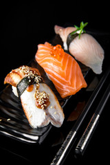 Nigiri Sushi Set of Unagi Eel, Sake Salmon, Tai Sea Bream Perch served on black plate, chopsticks and background.  Traditional Japanese cuisine. Wallpaper