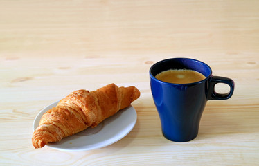 A Whole wheat croissant with a cup of hot coffee on the wooden table with free space for text and design 