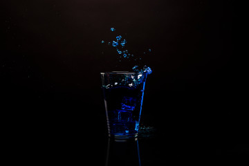 Glass blue drink splashing out. Shot against black reflective surface. Isolated beverage shot against black background. Copy space available