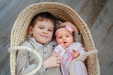 children, cute little boy 5 years old, with him newborn sister lies in a wicker cradle