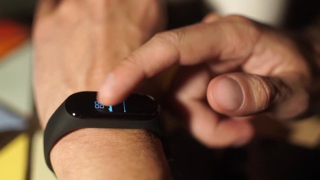 The man wore a fitness bracelet. Man checks pulse on fitness bracelet or activity tracker pedometer on wrist, sport, technology and healthy lifestyle concept, close up. Looks at the pedometer