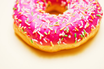 Bright donut in a pink glaze with a multi-colored rainbow sprinkle on a yellow background. 