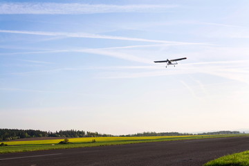 Unmanned aerial vehicle surveillance drone with light and camera landing on airport runway, ground, airfield, sunny summer morning, drone delivery concept, copy space on clear sky