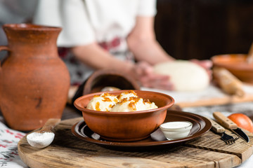 Ukrainian dumplings on a wooden board on the background of the hands of a baker