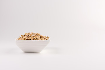 Dry rolled oatmeal in bowl isolated on white background.