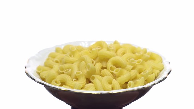 Raw macaroni in rotation. Elbow macaroni.  Macaroni rigati close up.  Raw pasta  isolated on white. Italian cuisine concept.