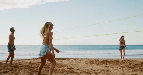 Active friends playing beach volleyball, athletic woman serves volleyball