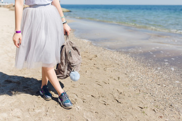 Girl with bag in hand standing on weat sand near sea. View of the legs in a lush gray skirt and...