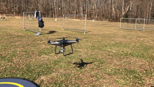 This Ultra High Definition footage is of a DJI Phantom 4 Pro drone that is hovering around a grassy field and lands on a pad.