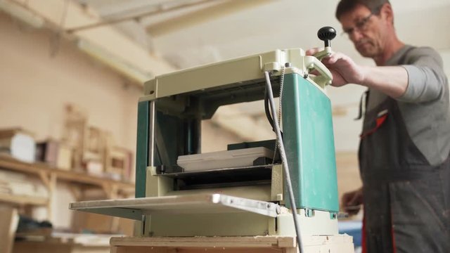 Professional furniture maker measuring wooden plank and sanding it with woodworking machine in his workshop