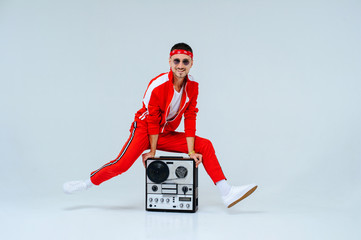 cheerful fashionable man wearing a red sports suit dancing jumps with a retro tape recorder....