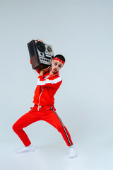 cheerful fashionable man wearing a red sports suit dancing jumps with a retro tape recorder. interesting and fervent style of the 90s
