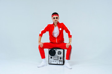 cheerful fashionable man wearing a red sports suit sitting with a retro tape recorder. proud and successful style of the 90's