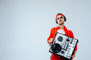 cheerful fashionable man wearing a red sports suit dancing jumps with a retro tape recorder....