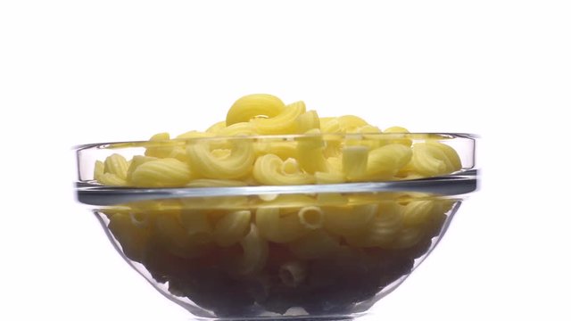 Raw macaroni in rotation. Elbow macaroni.  Macaroni rigati close up.  Raw pasta  isolated on white. Italian cuisine concept.