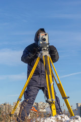 Surveyor conducts a topographical survey in winter for cadastral work at a construction site