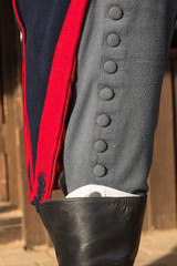 Details of a men's historical suit. The gray trousers with a number of large buttons filled in high hunting boots for riding, a long camisole of blue color with a red edging