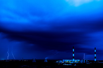 The cooling towers of thermal power station in the rainy night during the storm with the lightning