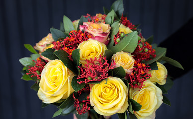 Stylish beautiful bouquet in yellow and coral colors of roses, Jatropha multifida and other plants in the florist hand.