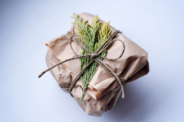 Small parcel on craft brown paper wrapping with hemp strap and junipers sprig. On white background.