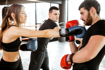 Fototapeta na wymiar Man and woman training to box with personal coach on the boxing ring at the gym