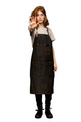 A full-length shot of a Young redhead woman with apron making stop gesture denying a situation that thinks wrong over isolated white background