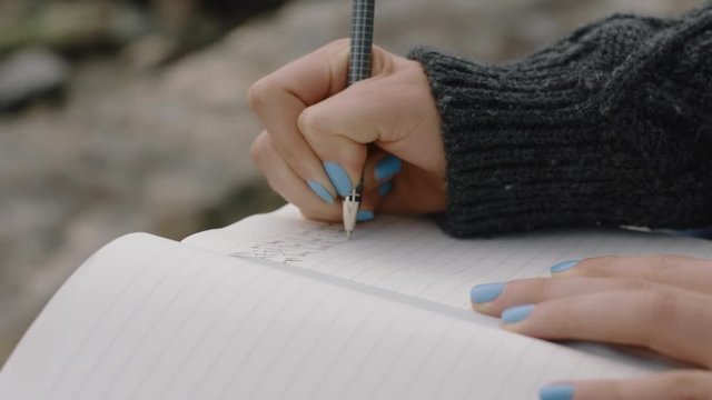 close up hands woman writing in diary journal teenage girl expressing lonely thoughts on seaside beach 