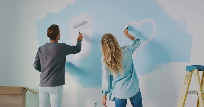 Smiling couple painting heart on wall, new home improvement