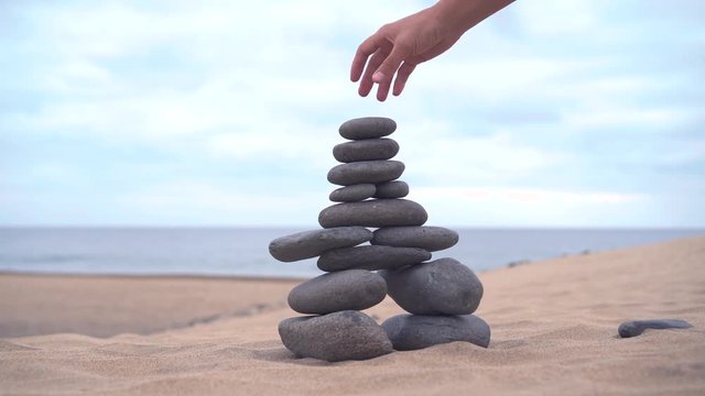 The cairn stands on the sand. The hand adds the last stone to finish the cairn. Sandy desert around