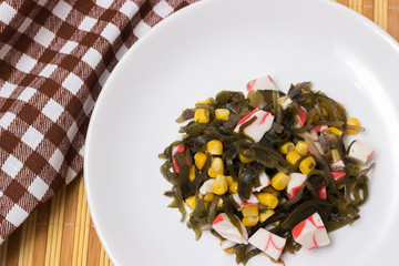 Salad of sea cabbage with crab and corn on a white plate